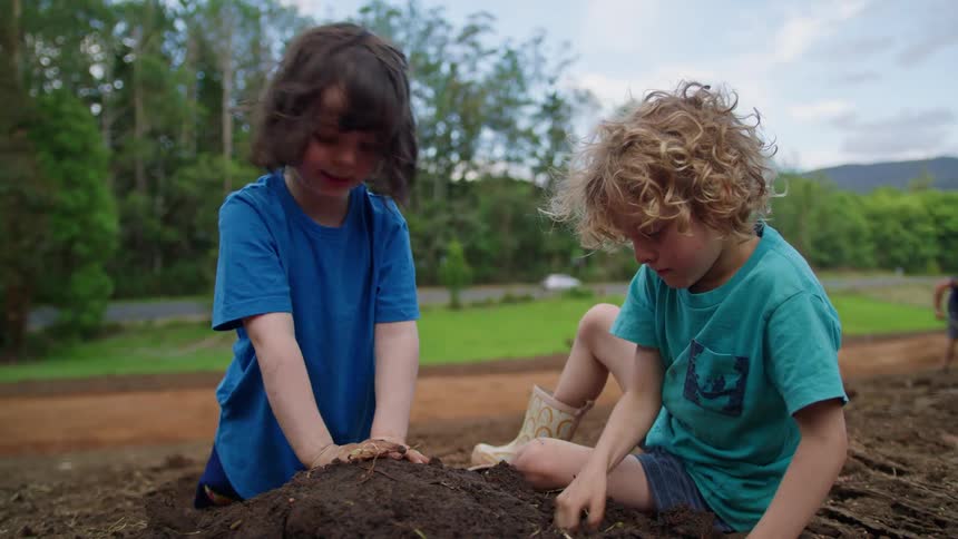 Toddler boy and girl playing on the ground next to a grass field and a road