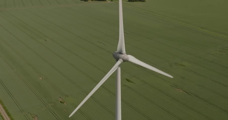 An aerial shot of a spinning wind turbine in the middle of empty green fields