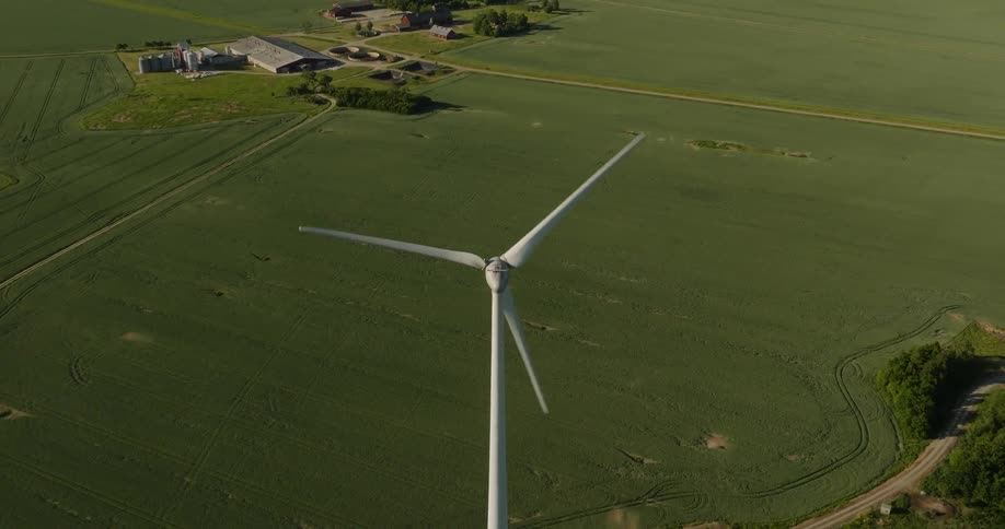 A wind turbine spins above a field in a rural area during the day