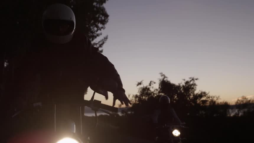 Two people stand while riding their motorcycles