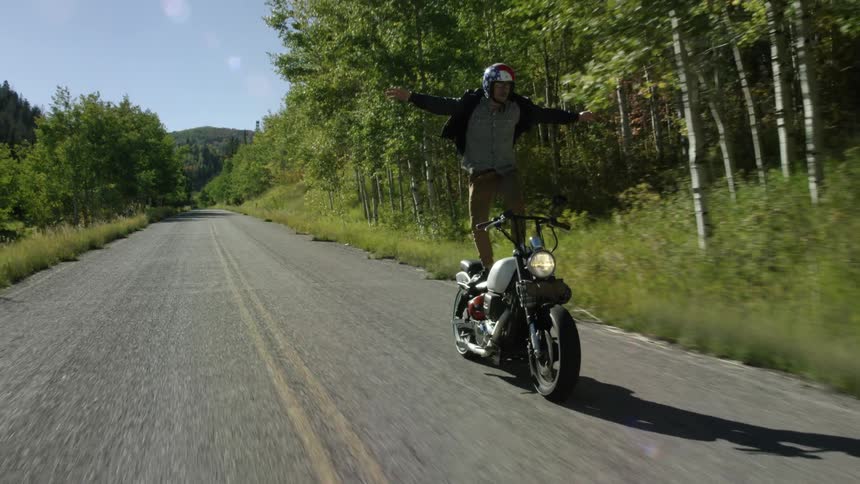 A man is standing on his moving motorcycle