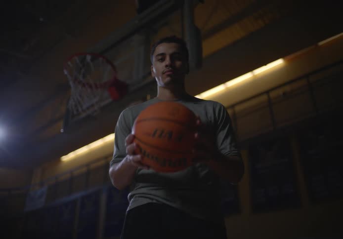 A young boy standing on a university basketball court holding a basketball in front of the hoop