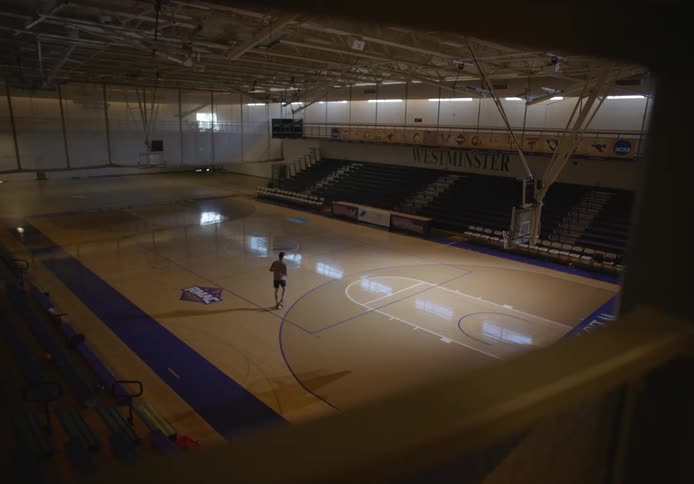 Young man in an empty university basketball court practicing his basketball shooting