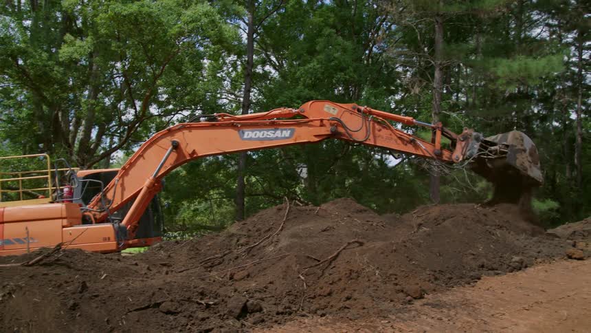 An excavator moves dirt in a field during the day
