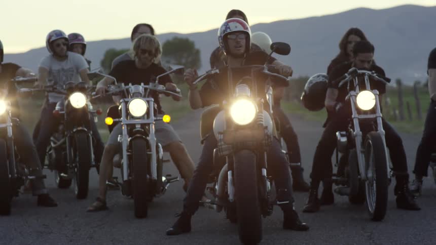 A group of people sit on motorcycles and turn their headlights on