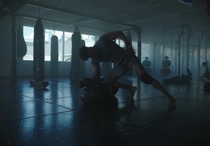 Black man in a mixed martial arts gym punching a dummy on the floor