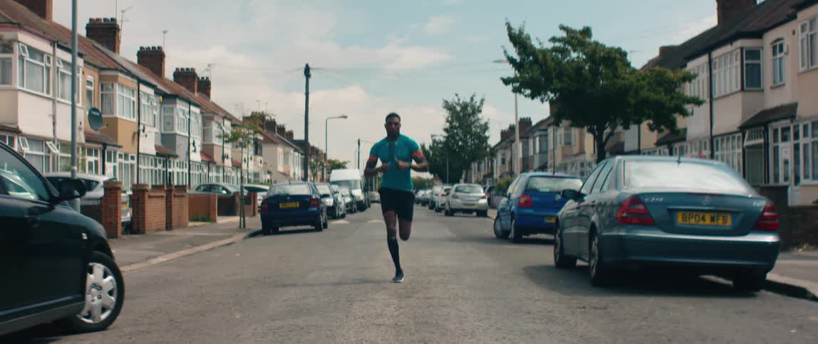 A man jogs down the street in a residential neighborhood during the day