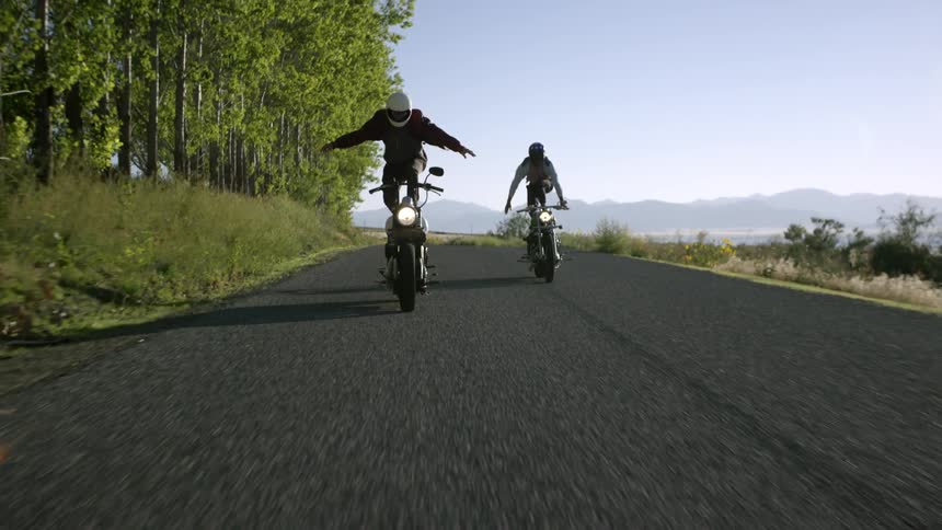Two people stand up while riding motorcycles down a road