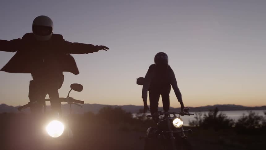 Two people stand up as they ride motorcycles