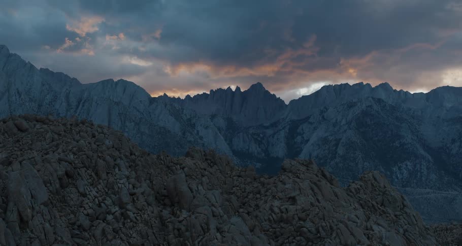 The sun peeks through dense clouds over a vast mountain range