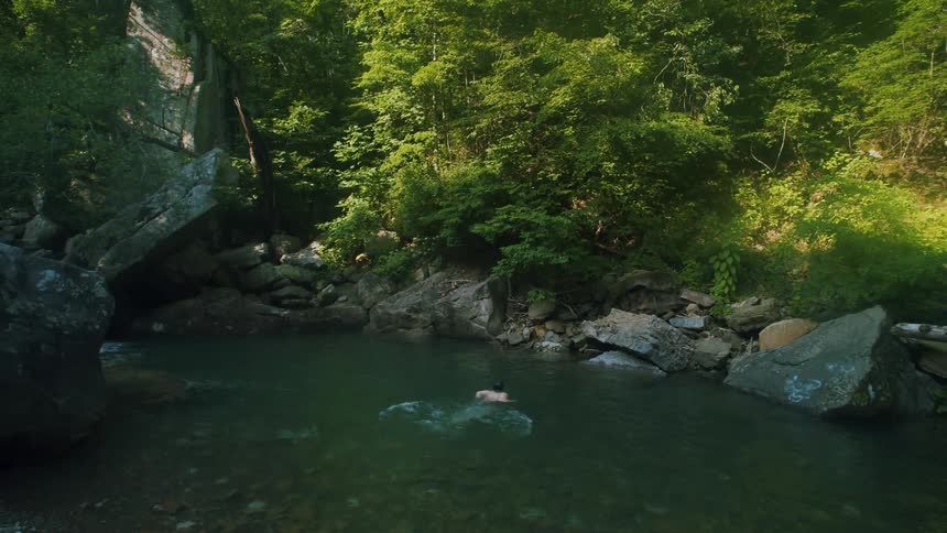 A man dives in a lake surrounded by large rocks and trees