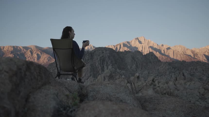 A female camper enjoys her morning coffee in the mountains