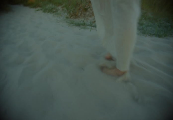 A woman walks along a sandy path as the camera follows her
