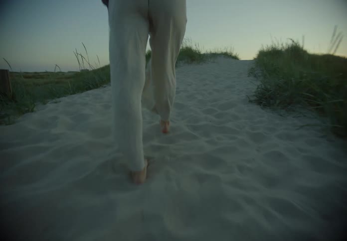 A woman walks along a sandy pathway that leads to a beach