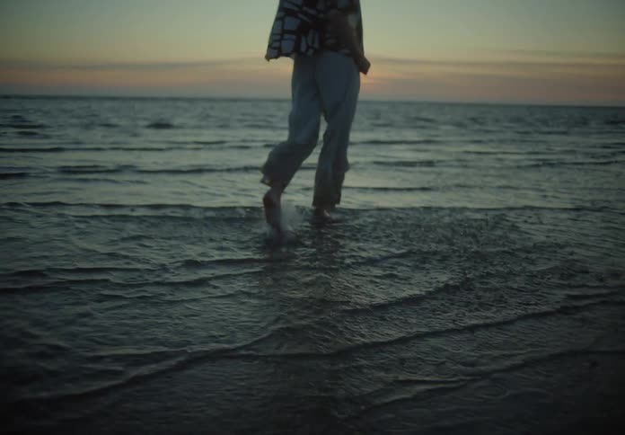 Person strolling through the beach water during sunset their clothes gently swaying in the breeze