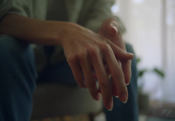 Woman with jeans and shirt sits on the couch in the living room hands touching each other