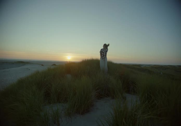 Against the backdrop of a stunning sunset a person stands atop a hill covered in pristine white sand donning a white shirt and pants the serene scene is bathed in warm hues creating a mesmerizing ambiance