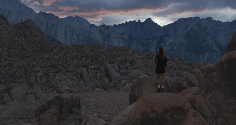 Woman in nature standing on top of a rock looking at a mountain area