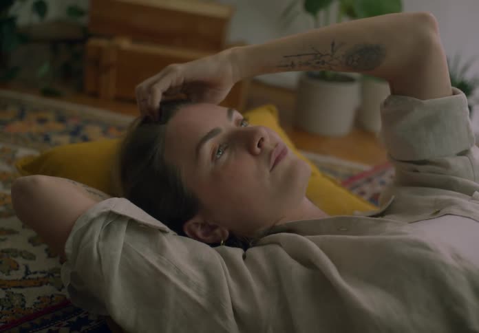 A woman runs her hand through her hair while lying on a carpet indoors