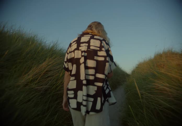 A woman walks a narrow path towards the beach