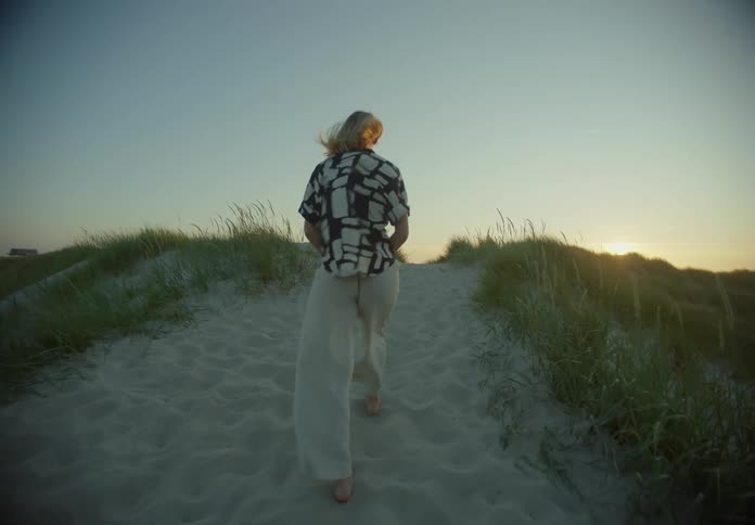 Blonde woman walking alone in the beach during dusk or dawn