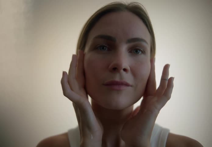 Woman smiles slightly while applying skin care product to her face