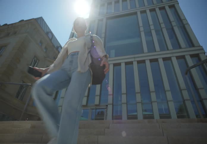 A woman descends a staircase outside of a building in a city on a sunny day