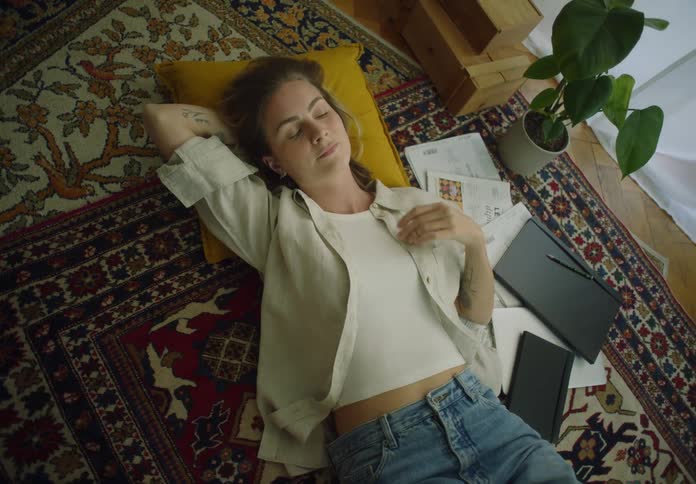 A woman lays on her back atop a rug as she looks around contemplatively