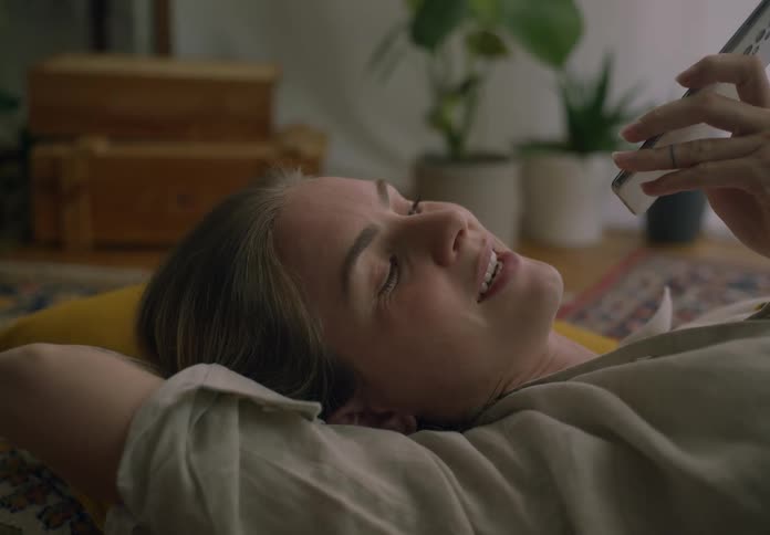 Woman lying on a cushion on the living room floor talking on the phone
