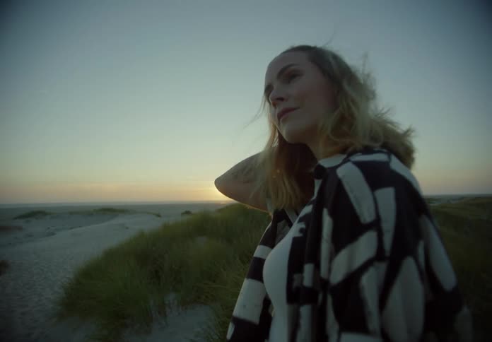 A woman stands in the sand at dusk