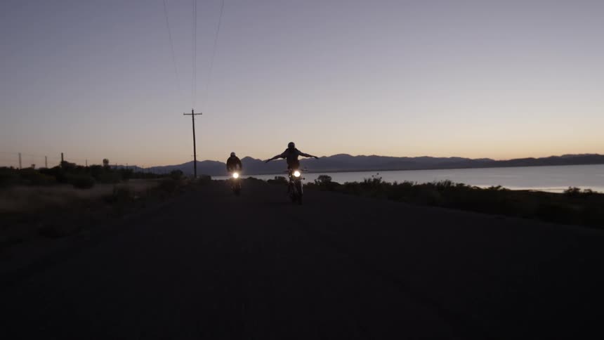 Two people do a trick standing on their motorcycle while driving