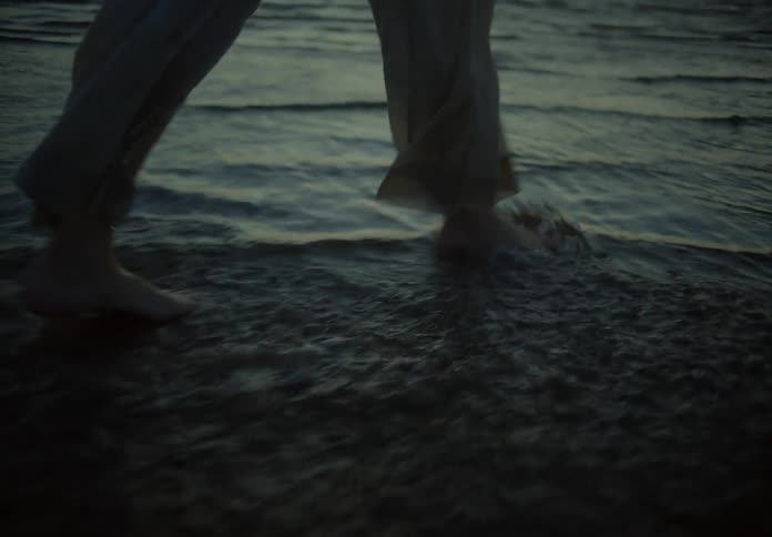Someones feet strolling and playfully splashing water on a beach during sunset