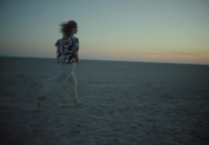 Woman runs across beach toward sun sitting on the horizon in a red sky