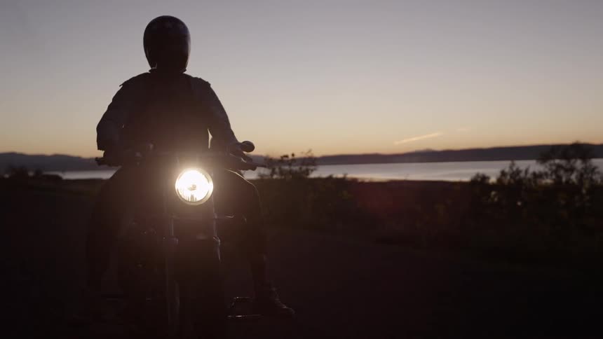 Motorcyclists ride near a lake at sunset