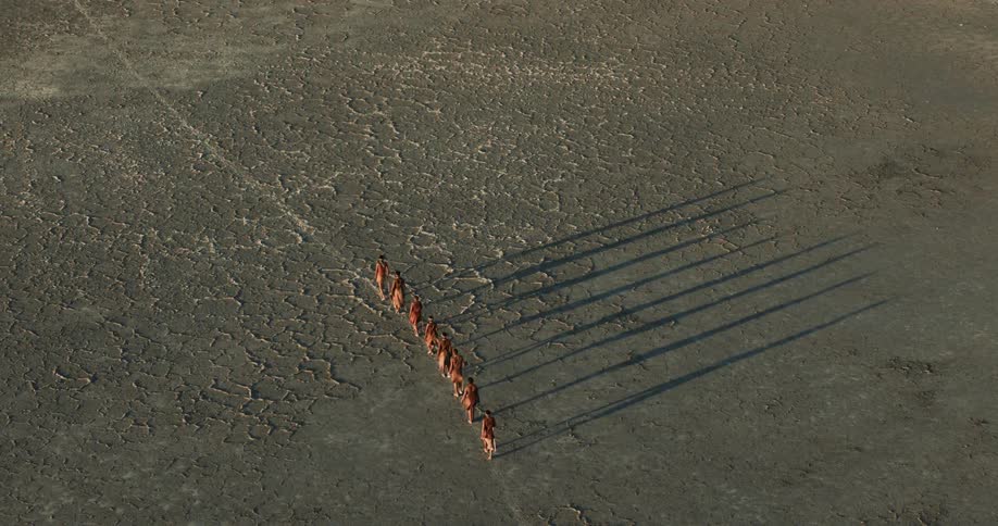 A group of bushmen are walking single file across a salt pan