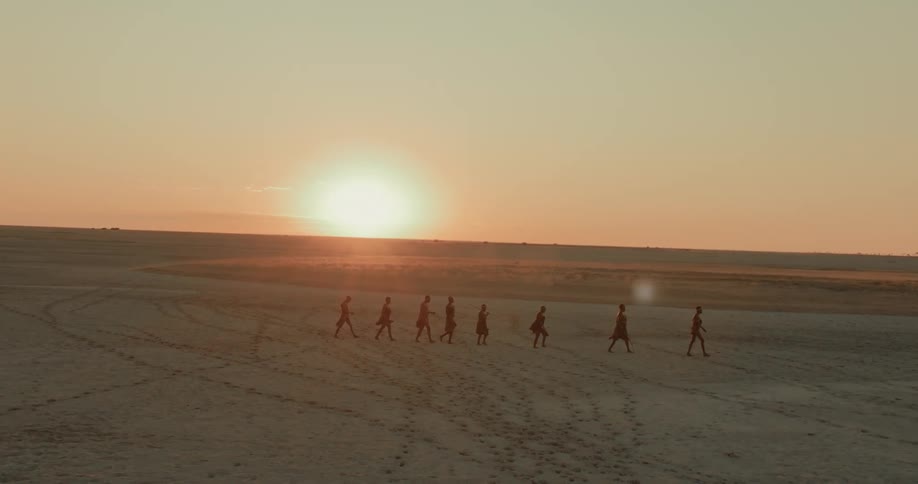 Bushmen are hiking in the desert at sunrise across a salt pan
