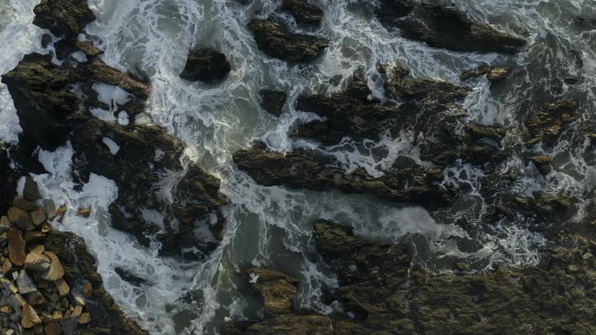 Aerial view of ocean waves breaking against the rocky shore