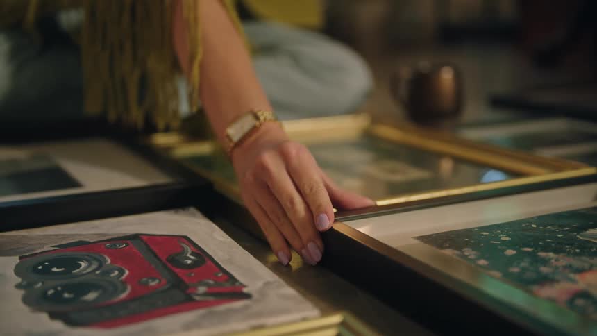 A young woman arranges several pieces of framed artwork located on the floor