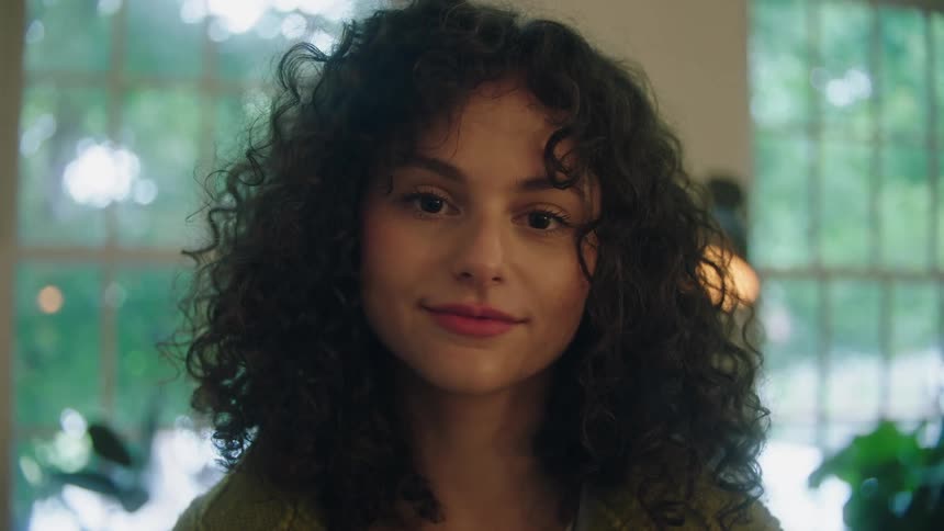 A young woman with very curly hair poses for the camera while indoors