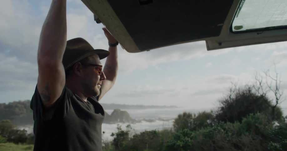 A man opens the rear door of a vehicle on the coast during the day