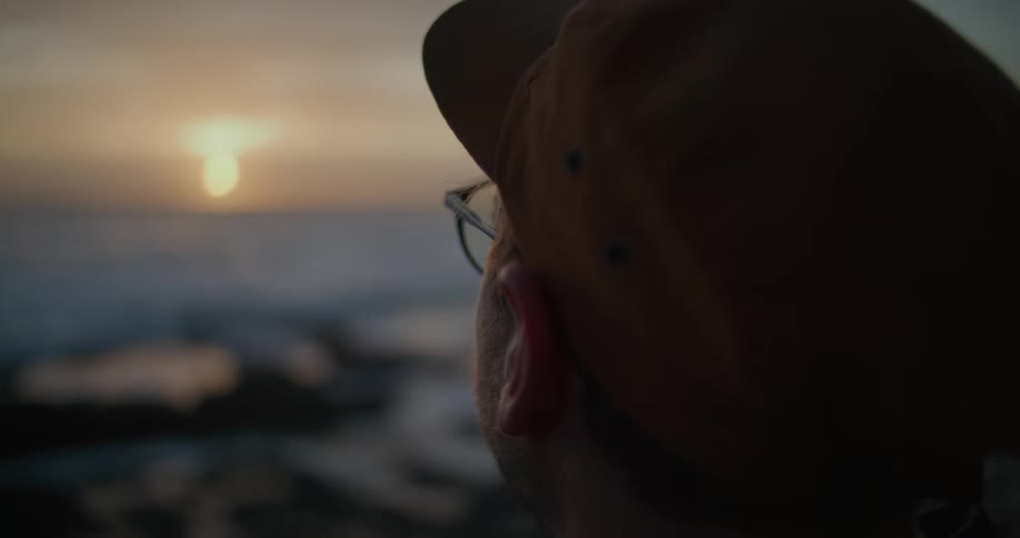 Man stands on shore looking toward sun on red horizon
