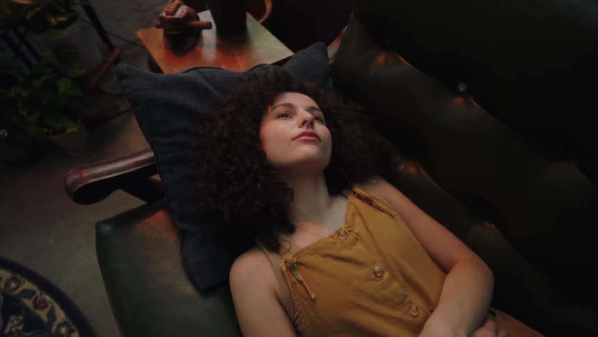 Restless and contemplative darkhaired woman lying down a couch