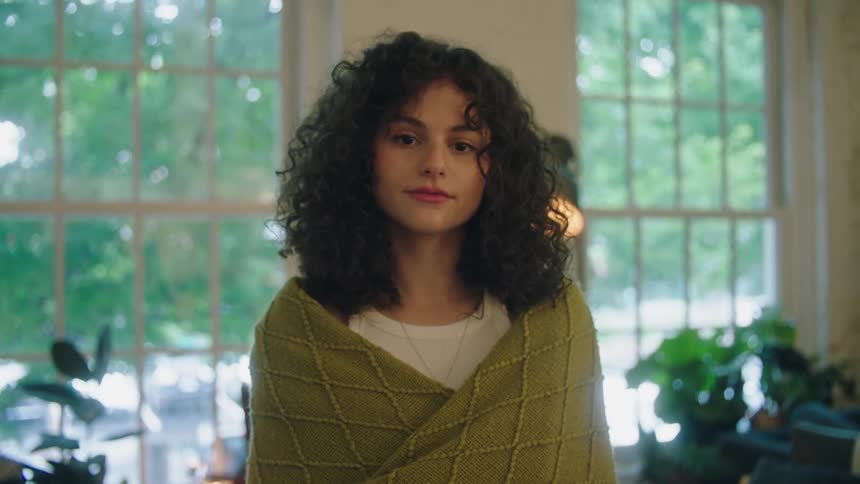 A young woman with very curly hair wraps herself in a knitted shawl