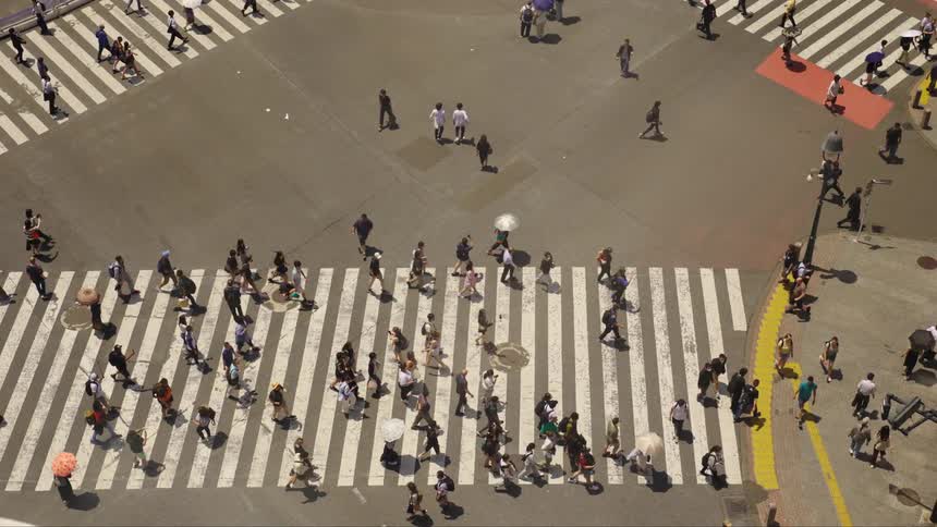 Numerous pedestrians crossing a busy Japanese street intersection on a sunny day