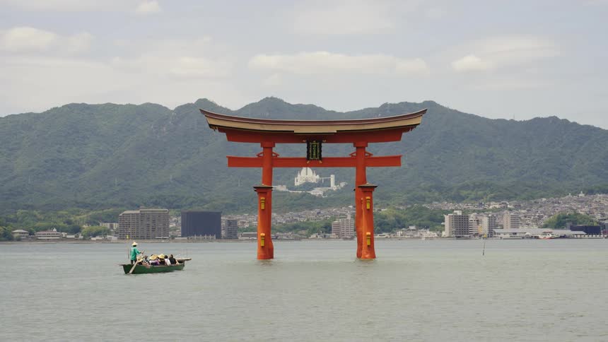 A rowboat sails toward the coast moving past a Japanese landmark