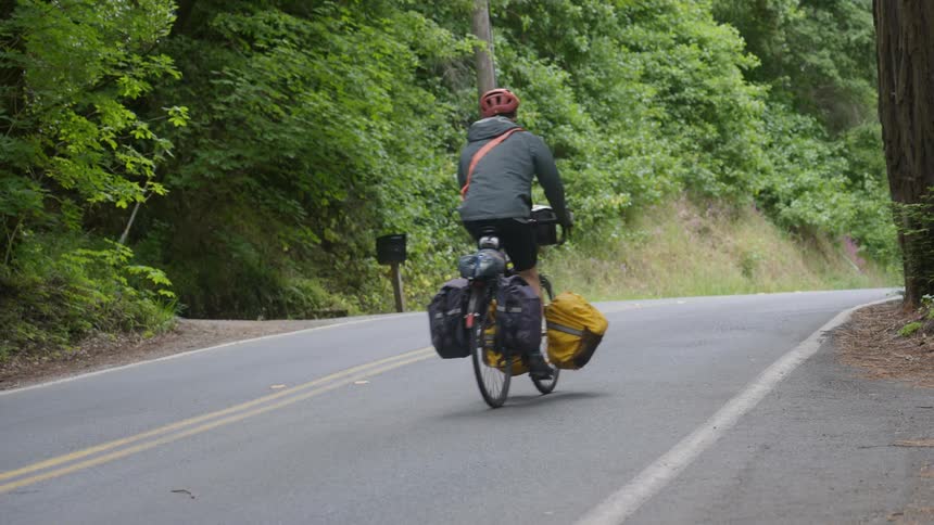 A man on a bicycle laden with many bags pedals along a road