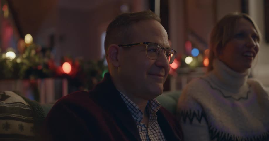 Father and daughter sitting on the living room couch surrounded by christmas lights enjoying each others company while watching tv