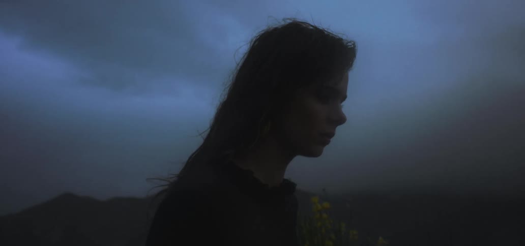 Woman stands outside with her eyes closed on gloomy overcast day with mountains in the background