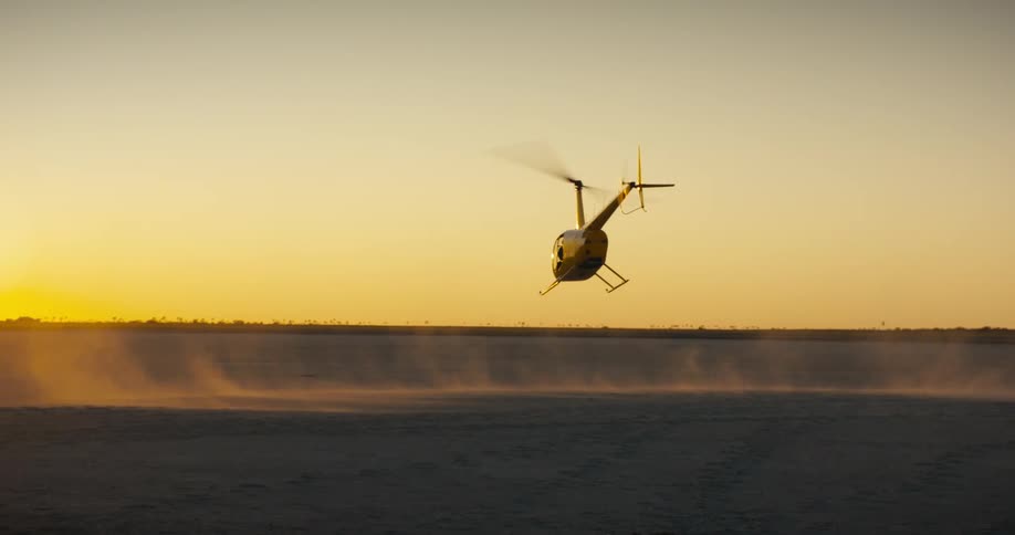 Yellow helicopter taking off in an open field during sunset