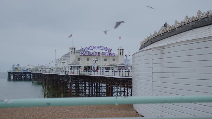 A pier with a white building in brighton england with seagulls flying over